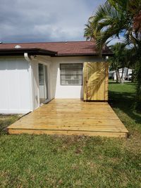 Newly constructed natural wood deck adjacent to a white residential building, featuring a privacy fence and tropical palm trees, crafted in Palm Bay.
