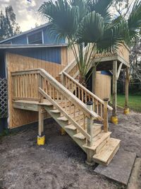 Newly constructed wooden staircase with railing leading to an elevated deck surrounded by lush palm trees, showcasing skilled woodwork in Brevard County.