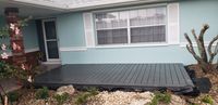Charcoal grey modern composite deck in front of a light blue house with a brick column, showcasing low-maintenance decking solutions in Florida.