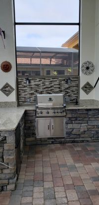 Elegant outdoor kitchen with stainless steel gas grill, stone cladding, and ambient lighting, exemplifying premium Palm Bay exterior designs.