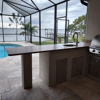 Waterfront outdoor kitchen with a granite bar overlooking a serene pool and lake, integrating luxury and nature in Palm Bay's exterior designs.