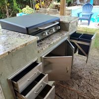Versatile outdoor kitchenette with a griddle and multiple drawers set against a tropical backdrop, illustrating the diverse exterior construction options available in Palm Bay and neighboring counties.