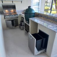 Sophisticated outdoor kitchen featuring a granite countertop, a high-end grill, and a ceramic egg smoker, highlighting Palm Bay's expertise in outdoor renovations.