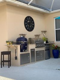 Elegant outdoor grilling station featuring a ceramic smoker and modern gas grill with built-in storage and decorative wall clock, crafted by a professional exterior design company in Palm Bay.