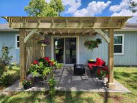 Charming wooden pergola over a cozy patio area with hanging flower baskets and potted plants, offering a relaxing outdoor retreat.