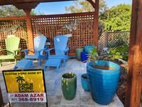 Cozy corner of a Palm Bay garden featuring a wooden pergola, colorful Adirondack chairs, and vibrant plant pots crafted by a local exteriors business.