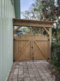 Double wooden gates under a pergola entryway, designed and installed by a top-rated Palm Bay exteriors company, enhancing Florida home curb appeal.