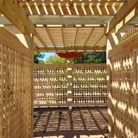 Inside view of a custom-built pergola by Palm Bay exterior professionals, with sunlight casting shadows through slatted roof over a welcoming 'Sunflower' sign.