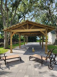 Wooden pavilion with a sturdy gabled roof over a paved patio, offering a serene outdoor sitting area by a Palm Bay exterior design company.