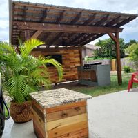 Rustic outdoor kitchen pavilion with a shingle roof and wooden bar in Brevard County, FL, showcasing expertise in backyard entertainment spaces.