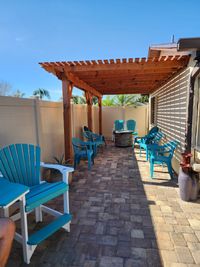 Inviting patio space with a red-stained wooden pergola and vibrant blue Adirondack chairs, highlighting Palm Bay's outdoor living solutions.